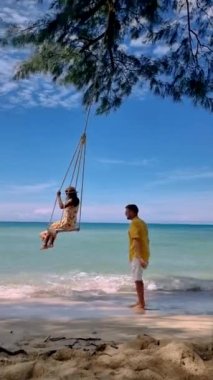 Couple of men and women playing at a swing on the beach of Koh Kood in Thailand.