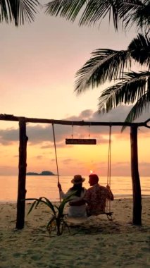 Couple of men and women at a swing on the beach of Koh Chang Island in Thailand during sunset.