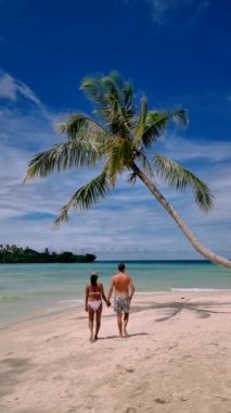 couple on a tropical beach during vacation at the Island of Koh Kood in Thailand, men and women on a white beach with palm trees. 