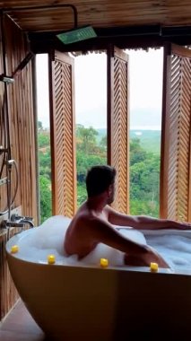 men in a bathtub at a bamboo hut in the mountains of Phangnga Thailand looking out over the ocean Samthnangshe viewpoint. 
