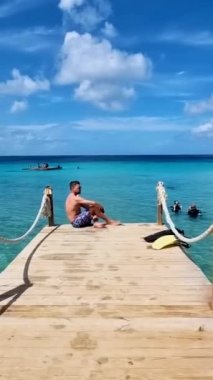 young men in swim short sitting on a wooden bier at Curacao Caribbean Island, Kokomo Beach of Curacao. 