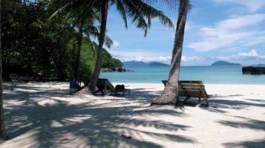 Tropical beach in Thailand with palm trees and black stones in the ocean of Koh Kham near Koh Mak. 