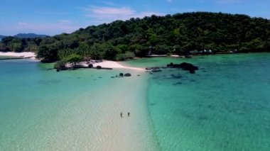 couple at a Tropical beach in Thailand with black stones in the ocean of Koh Kham near Koh Mak, men and women at a sandbank in turqouse colored ocean