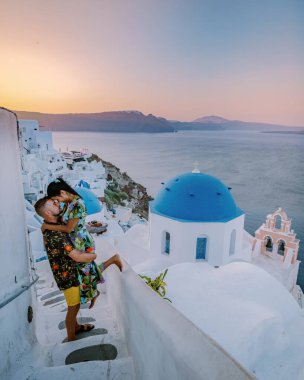 Santorini Greece, young couple mid age European and Asian on vacation at the Greek village of Oia Santorini Greece, luxury vacation Santorini. mid age man and woman watching sunset Santorini clipart