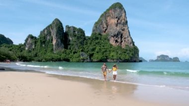 couple of men and women on a tropical white beach in Thailand, Railay Beach Krabi during summer vacation in Thailand with limestone cliffs on the background