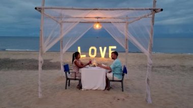 a couple of men and women having a romantic dinner on a tropical white beach in Thailand in the evening.