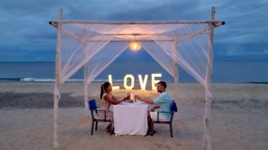 a couple of men and women having a romantic dinner on a tropical white beach in Thailand in the evening.