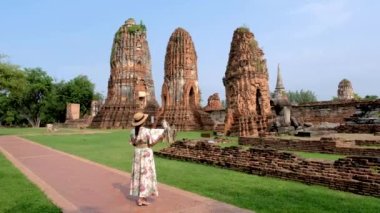 Asian women with a tourist map in hand looking at the ruins and Pagodas at Wat Mahathat Temple of Ayutthaya Province. Ayutthaya Historical Park, Thailand. 