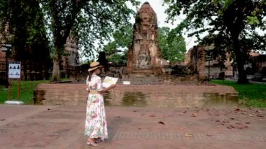 Asian women with a tourist map in hand looking at the ruins and Pagodas at Wat Mahathat Temple of Ayutthaya Province. Ayutthaya Historical Park, Thailand. 