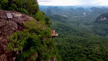 Ejderha Tepesi dağı Krabi Tayland, genç bir gezgin uçurumun üzerindeki kayanın üzerinde oturuyor, güzel bir manzarası var. Tayland, Krabi 'deki Khao Ngon Nak Doğa Yolu' nda Ejder Tepesi veya Khuan Sai..
