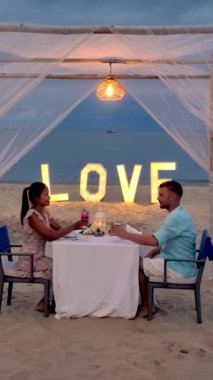 a couple of men and women having a romantic dinner on a tropical white beach in Thailand in the evening.