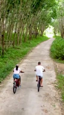 couple on a bike in the countryside in Thailand bicycling between rubber planation trees. 