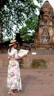 Asian women with a tourist map in hand looking at the ruins and Pagodas at Wat Mahathat Temple of Ayutthaya Province. Ayutthaya Historical Park, Thailand. 