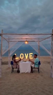 a couple of men and women having a romantic dinner on a tropical white beach in Thailand in the evening.
