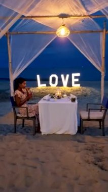 a couple of men and women having a romantic dinner on a tropical white beach in Thailand in the evening.