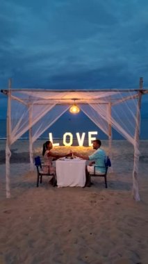 a couple of men and women having a romantic dinner on a tropical white beach in Thailand in the evening.