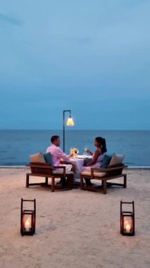 a couple of men and women having a romantic dinner on a tropical white beach in Thailand in the evening.