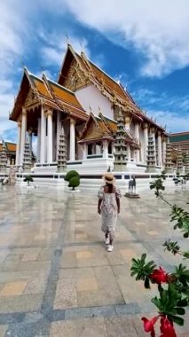 A couple of men and women visit a Thai Buddhist temple in Bangkok Thailand, Wat Suthat, better known for the towering red Giant Swing that stands at its entrance, is one of the oldest and most