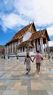 A couple of men and women visit a Thai Buddhist temple in Bangkok Thailand, Wat Suthat, better known for the towering red Giant Swing that stands at its entrance, is one of the oldest and most