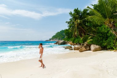 Young men in a swim short on a white tropical beach with palm trees Petite Anse beach Mahe Tropical Seychelles Islands. 