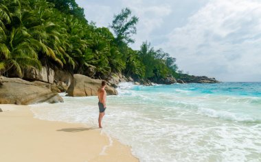 Young men in swim short on a white tropical beach with palm trees Petite Anse beach Mahe Tropical Seychelles Islands. 