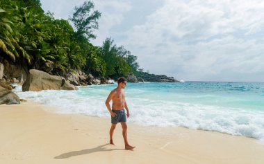 Young men in a swim short on a white tropical beach with palm trees Petite Anse beach Mahe Tropical Seychelles Islands on a sunny day