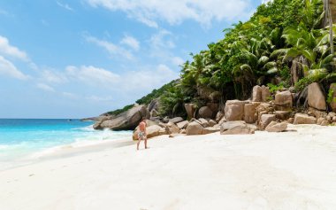 A young man in a swim short on a white tropical beach with huge boulders and palm trees Coco Island Tropical Seychelles Islands. 