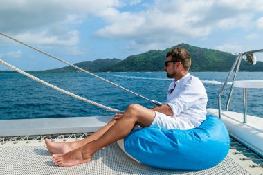 Young men on a trip with a Sailing boat at the Tropical Seychelles Islands.