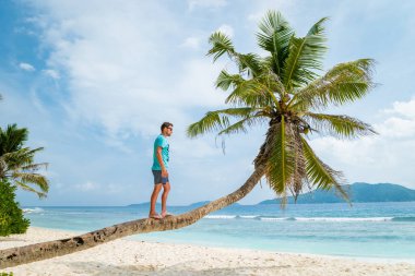 Young men relaxing at a palm tree on a tropical white beach at the La Digue Seychelles Islands. 