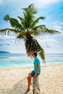 Young men relaxing at a palm tree on a tropical white beach at the La Digue Seychelles Islands. 