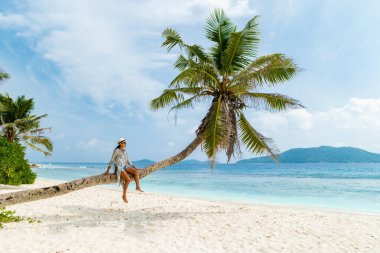 Young woman relaxing at a coconut palm tree on a white tropical beach at La Digue Seychelles Islands. 