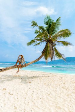 Young woman relaxing at a coconut palm tree on a white tropical beach at La Digue Seychelles Islands. 