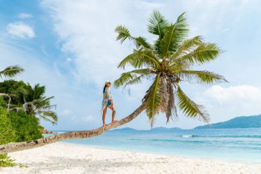 Asian woman relaxing at a coconut palm tree on a white tropical beach at La Digue Seychelles Islands. 