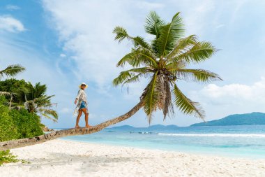 Asian woman relaxing at a coconut palm tree on a white tropical beach at La Digue Seychelles Islands. 