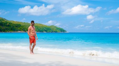 Young men in a swim short at Anse Lazio beach with turquoise colored ocean Praslin Seychelles Islands.