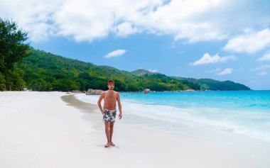 Young men in a swim short relaxing at Anse Lazio beach with turquoise colored ocean Praslin Seychelles Islands.