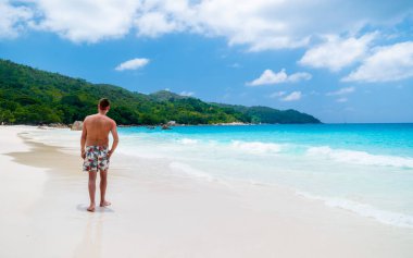 Young men in a swim short relaxing at Anse Lazio beach with turquoise colored ocean Praslin Seychelles Islands.