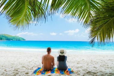 Couple relaxing under a palm tree on a white tropical beach Anse Lazio Praslin Tropical Seychelles Islands. 