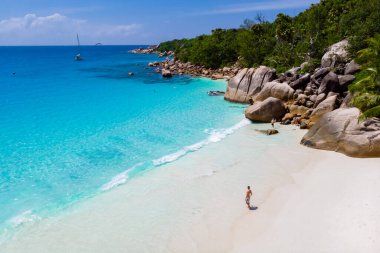 young men on a white beach with turquoise colored ocean, Drone view from above at Anse Lazio beach Praslin Island Seychelles.