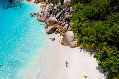 young men on a white beach with turquoise colored ocean, Drone view from above at Anse Lazio beach Praslin Island Seychelles.