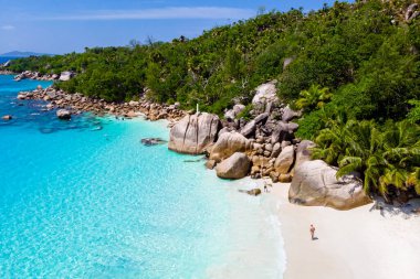 young men on a white beach with turquoise colored ocean, Drone view from above at Anse Lazio beach Praslin Island Seychelles.