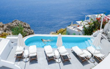 men relaxing in an infinity swimming pool during vacation at Santorini, swimming pool looking out over the Caldera ocean of Santorini, Oia Greece, Greek Island Aegean Cyclades luxury vacation. 