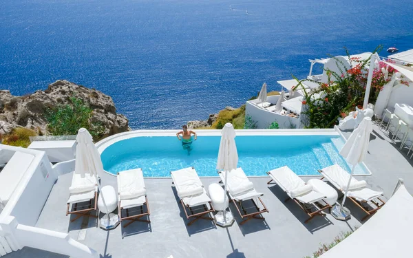 men relaxing in an infinity swimming pool during vacation at Santorini, swimming pool looking out over the Caldera ocean of Santorini, Oia Greece, Greek Island Aegean Cyclades luxury vacation.
