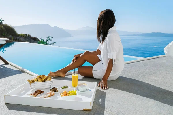 Happy women having breakfast by the infinity pool looking out over the Caldera ocean of Santorini Greece on vacation