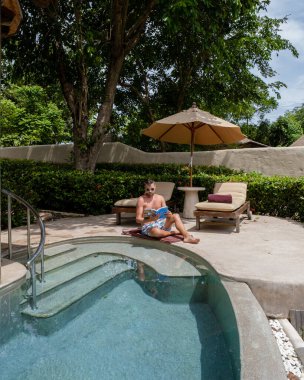 young men reading a book at a pool, young men in swim short at a swimming pool