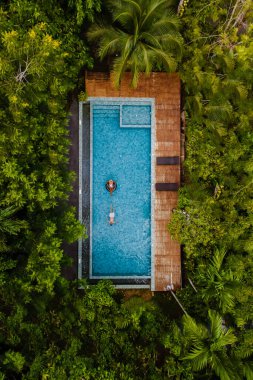 drone view of a swimming pool in the jungle, aerial view from a drone above a swimming pool in the rainforest, men and women in a pool