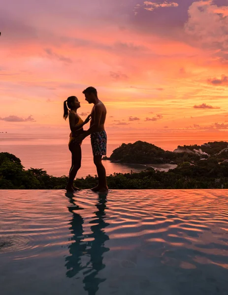 熱帯の島で休暇中にスイミングプールでロマンチックな男女のカップル 日没時にインフィニティプールの男と女 豪華なプールヴィラでの贅沢な休暇 — ストック写真