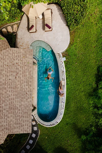 熱帯の島で休暇中にスイミングプールで若い男女のカップルで上からのドローンビュー インフィニティプールの男と女豪華なプールヴィラでの贅沢な休暇 — ストック写真