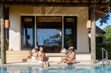 Men working at a laptop a digital nomad working at a swimming pool during a vacation on a tropical island. man and woman in the infinity pool during sunset. luxury vacation in a luxury pool villa