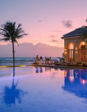 a young couple of men and women at a swimming pool during a vacation on a tropical island watching the sunset on a tropical beach
